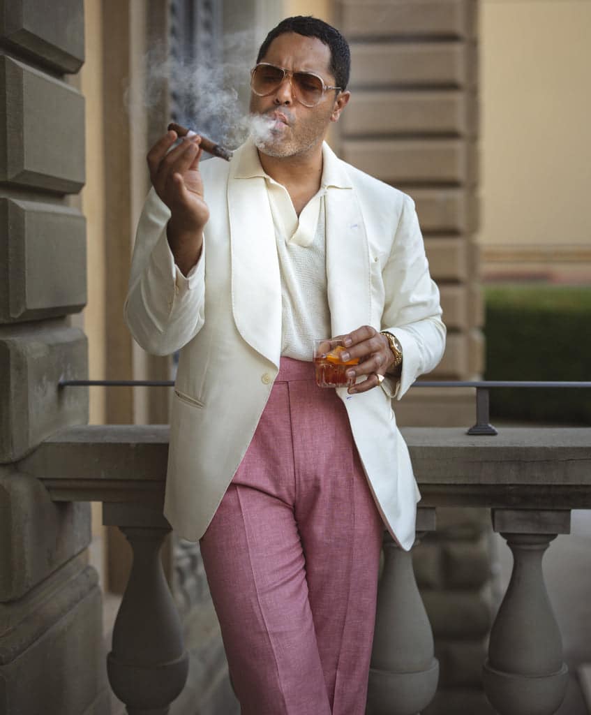 Angel Ramos smoking a cigar while sipping an aperitivo, dressed in a cream blazer and pink trousers at Pitti Uomo.