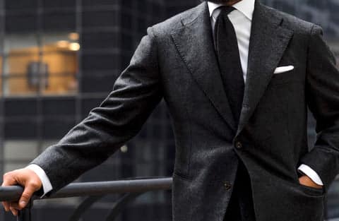Man in a dark charcoal suit, white dress shirt, and black tie, showcasing an elegantly tailored look with a perfectly tied Four-In-Hand knot.