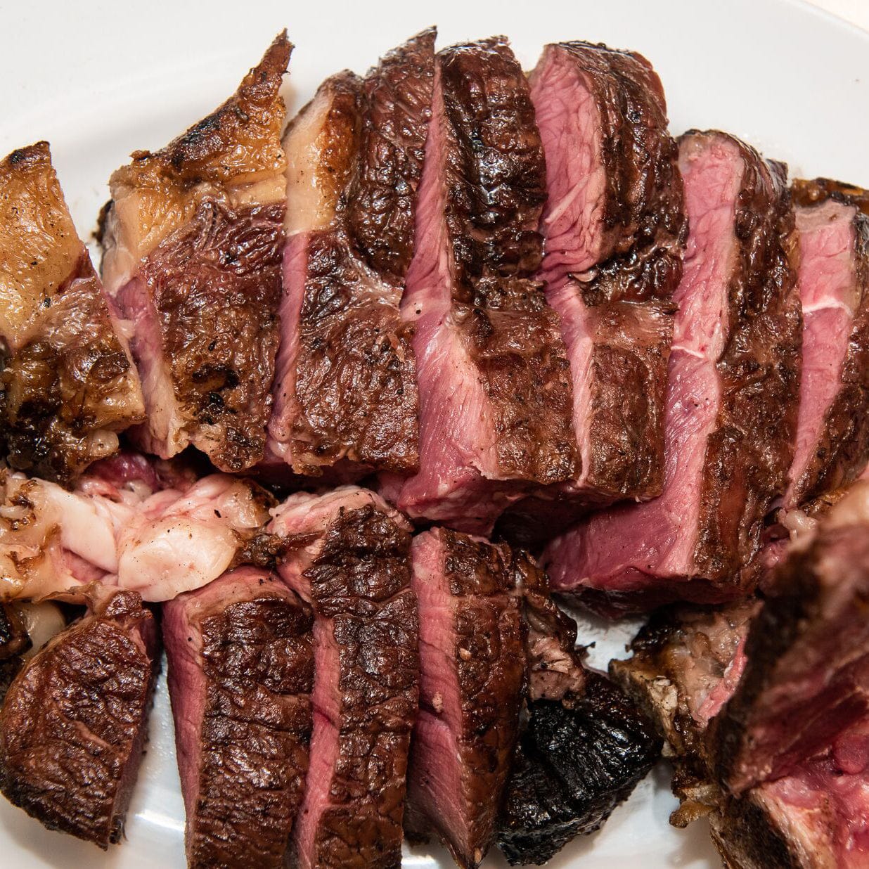Traditional Bistecca alla Fiorentina steak, sliced to reveal its perfectly rare center, served on a white plate.
