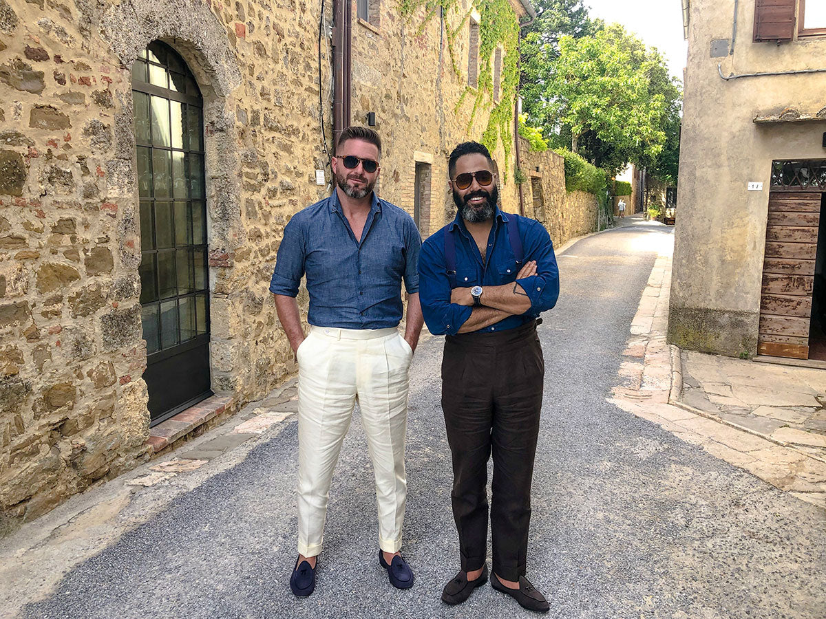 Angel Ramos and Stephen standing in a rustic European alleyway, both dressed in summer-appropriate menswear.