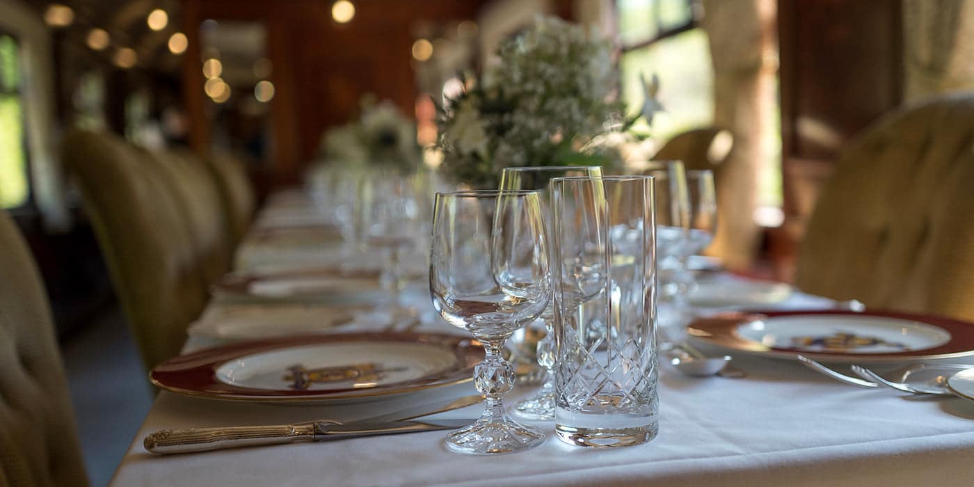 A close-up of crystal glassware and fine china on a vintage train’s elegant dining table.