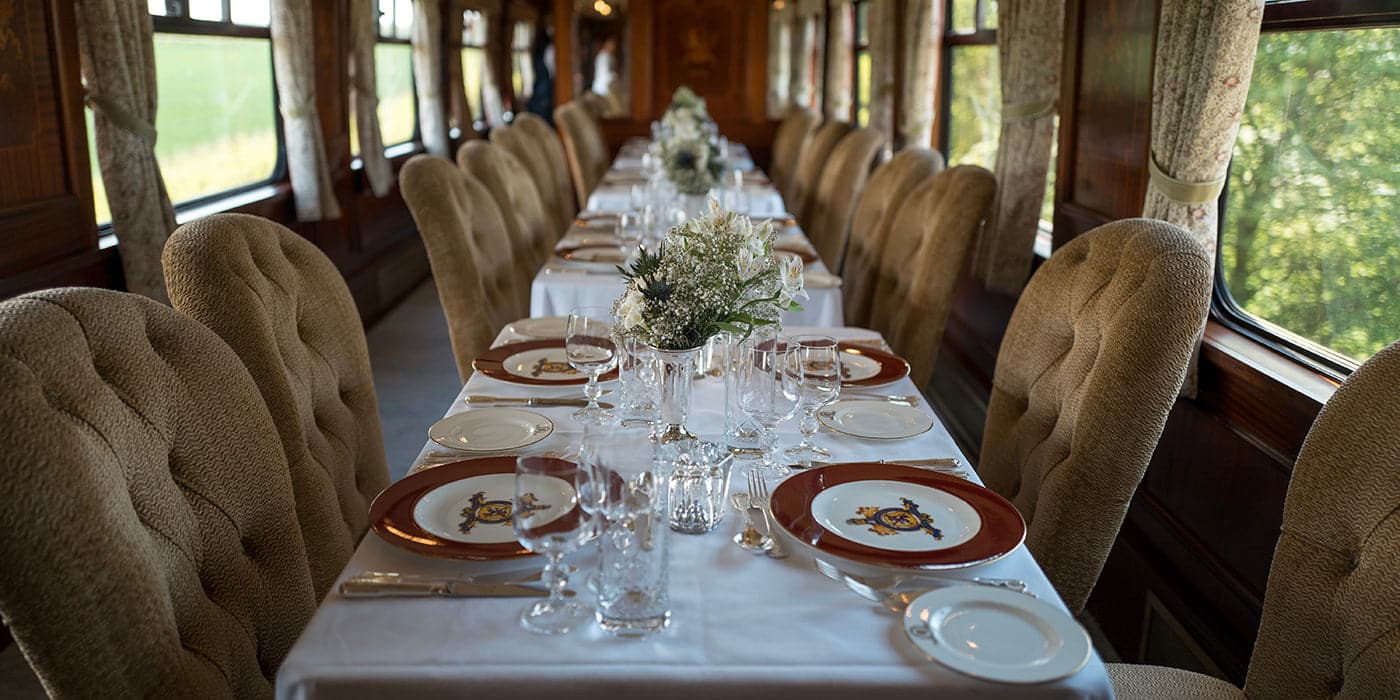 A luxurious dining setup inside a vintage train, featuring fine china, crystal glassware, and floral centerpieces.