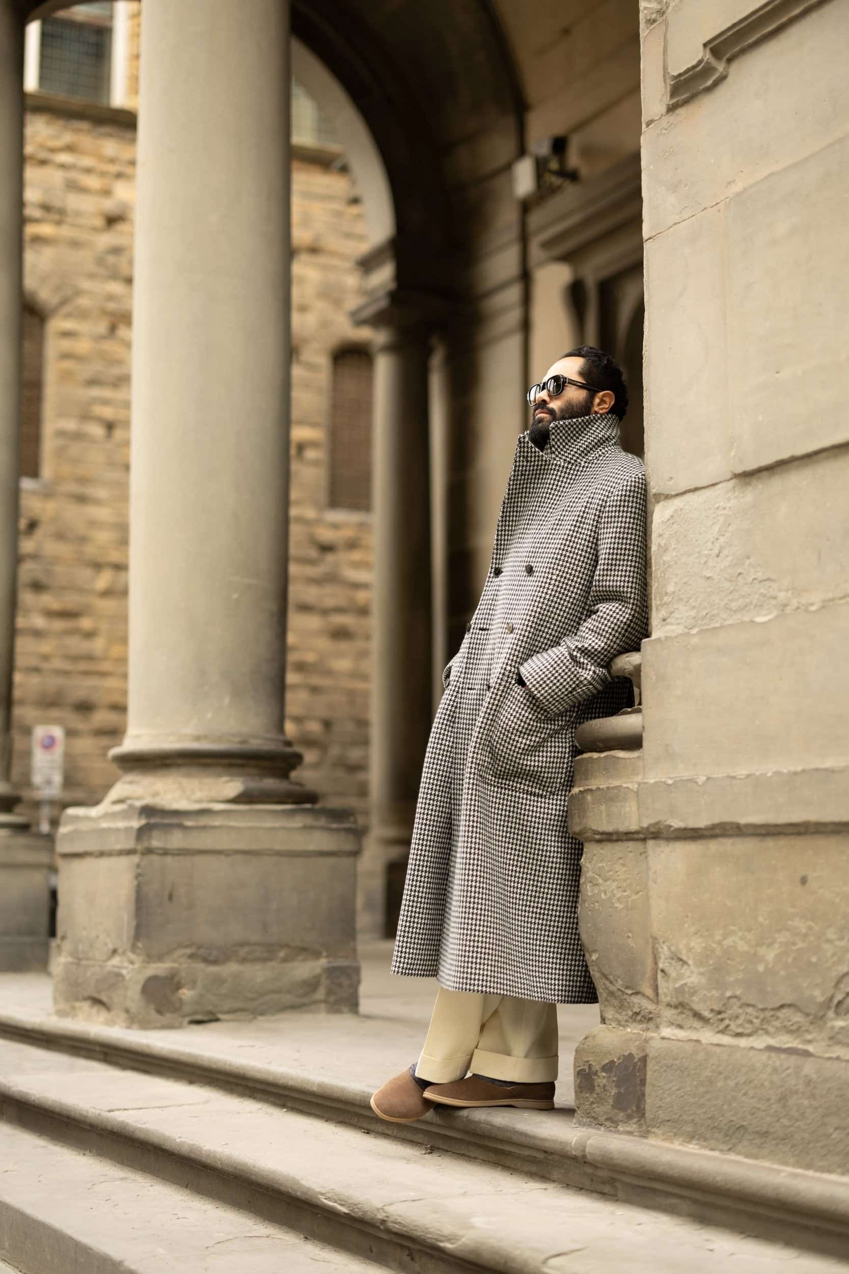 Angel Ramos leans against a stone column in Florence, Italy, wearing a black and white houndstooth overcoat.